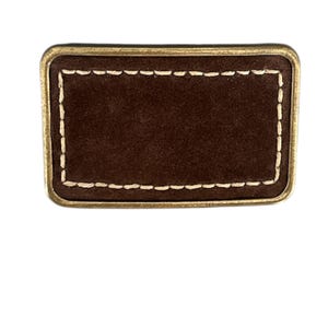 May include: A brown leather patch with a gold border and white stitching. The patch is rectangular and has a blank surface.