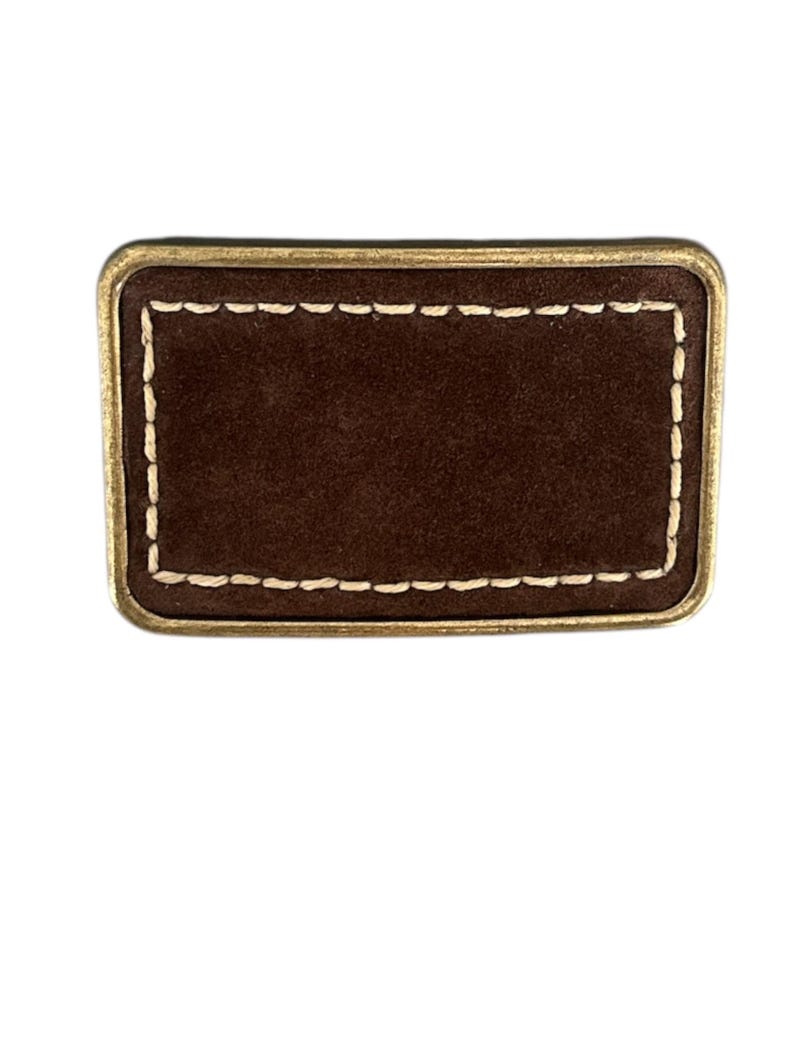 May include: A brown leather patch with a gold border and white stitching. The patch is rectangular and has a blank surface.