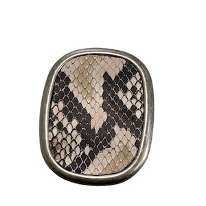 May include: A silver-toned belt buckle with a snakeskin pattern in shades of brown, beige, and black.
