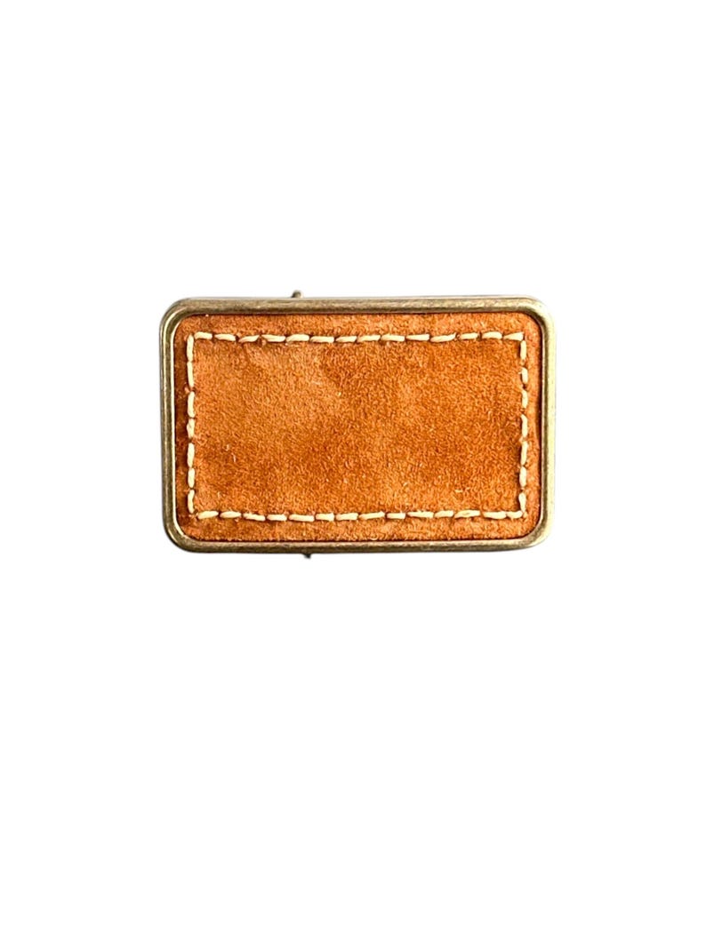 May include: A rectangular brown leather patch with a stitched border. The patch is surrounded by a metal frame.