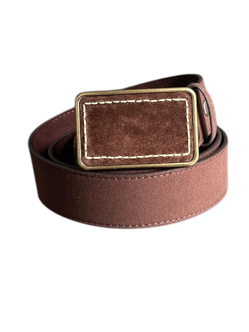 May include: A brown suede belt with a brass buckle. The buckle has a suede insert with a stitched border.