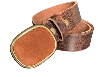 Könnte beinhalten: Ein brauner Ledergürtel mit einer rechteckigen Schnalle. Die Schnalle hat einen goldfarbenen Rahmen und eine braune Wildleder-Mitte. Der Gürtel hat ein Used-Finish und ist aufgerollt.