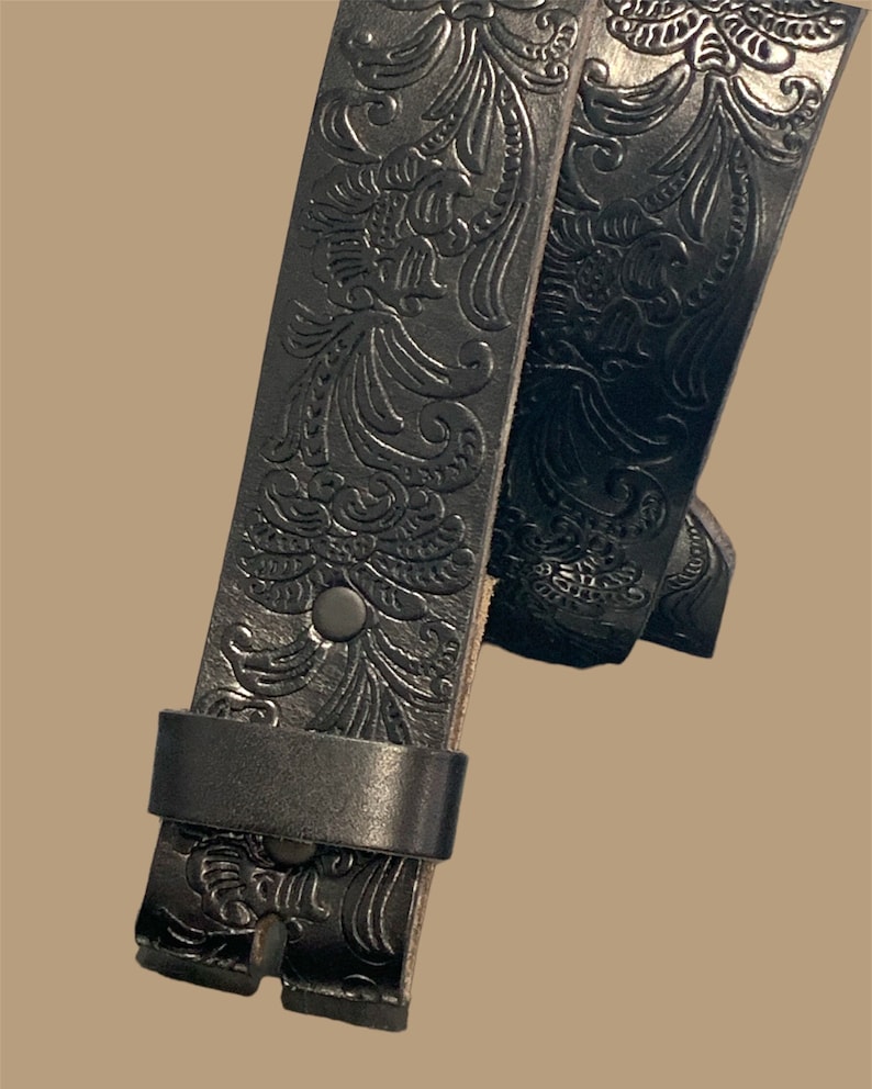 K&ouml;nnte beinhalten: Schwarzer Lederg&uuml;rtel mit einem gepr&auml;gten Blumenmuster. Der G&uuml;rtel ist in der Mitte gefaltet, wodurch das Detail des Musters sichtbar wird.