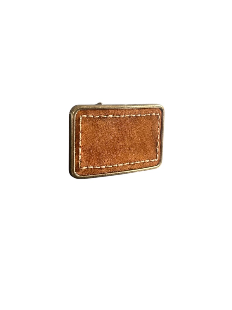 May include: A brown leather belt buckle with a stitched border. The buckle is made of metal and has a rectangular shape.