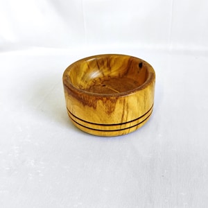 May include: A small, round wooden bowl with a natural wood finish. The bowl has two dark brown bands around the rim.