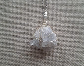 May include: A silver necklace featuring a light gray crystal pendant. The crystal is wrapped in silver wire and suspended from a delicate chain. The pendant has a rough, natural texture, and the overall design is simple and elegant.