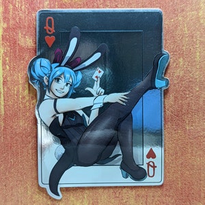 May include: A silver sticker featuring a cartoon illustration of a woman with blue hair wearing a black and white bunny costume and holding a playing card. The card is red with a white heart and the number two on it. The sticker has a silver background and a white border. The text "Q" and a red heart are in the top left corner of the sticker.