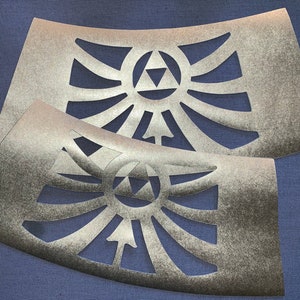 Puede incluir: Dos plantillas de color plateado con un diseño triangular y un patrón de rayos de sol. Las plantillas están sobre un fondo azul.