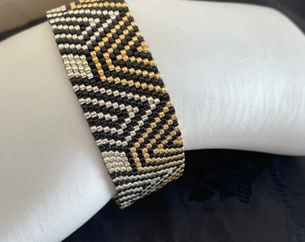 May include: A black, silver, and gold beaded bracelet with a geometric pattern.