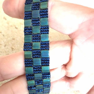May include: A blue and green beaded bracelet with a checkered pattern.