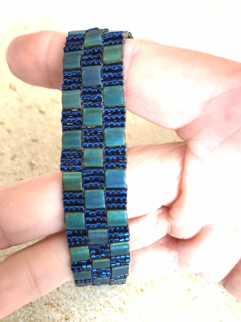May include: A blue and green beaded bracelet with a checkered pattern.