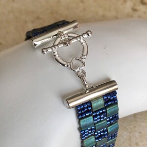 May include: A blue and green beaded bracelet with a silver toggle clasp. The clasp has a heart-shaped detail.