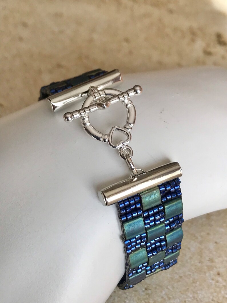 May include: A blue and green beaded bracelet with a silver toggle clasp. The clasp has a heart-shaped detail.