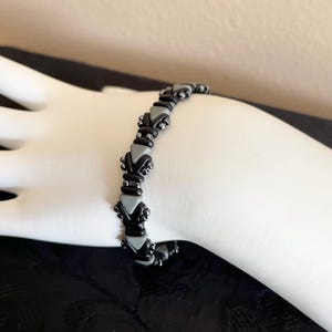 May include: A black and gray beaded bracelet with a geometric pattern. The bracelet is made with small, triangular beads.
