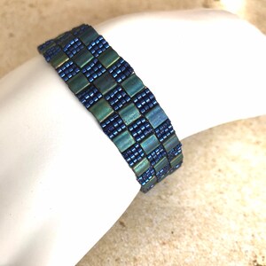 May include: A blue and green beaded bracelet with a checkered pattern.