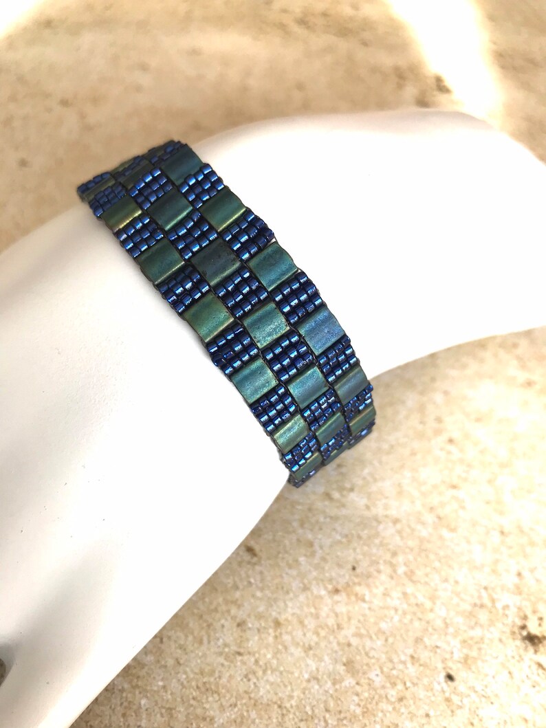 May include: A blue and green beaded bracelet with a checkered pattern.