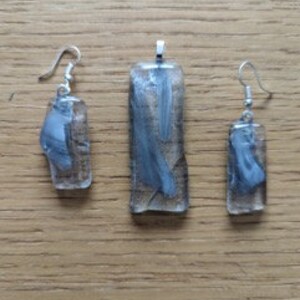 Peut inclure: Un ensemble de trois boucles d'oreilles en verre et un collier avec un pendentif. Le verre est transparent avec un motif marbré gris et blanc. Les boucles d'oreilles et le pendentif sont de forme rectangulaire.