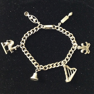 Peut inclure: Un bracelet à breloques en argent avec une variété de breloques, dont une cloche, une harpe, une fleur de lys et une petite figurine d'animal.