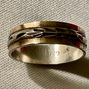 May include: A silver ring with a textured, patterned band. The ring has a gold-colored edge and the interior is stamped with "925 18K". The ring is a piece of jewelry.