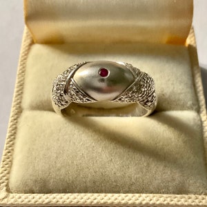 Peut inclure: Une bague en argent avec une bande texturée et un dessus bombé serti d'une seule pierre rouge.
