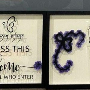 May include: Two framed wall art pieces. The left frame has text that reads "BLESS THIS HOME" with floral accents. The right frame features a line drawing of a man with a turban and a decorative letter. The artwork is in black frames.