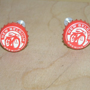 May include: Two red bottle caps with a white bicycle logo and the text "New Belgium Brewing" on each cap.