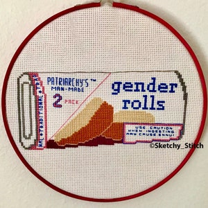 Puede incluir: Una bordado de punto de cruz de una etiqueta de producto de parodia para "gender rolls" con el texto "Patriarchy's TM Man-Made 2 Pack" y "Use Caution: When Ingesting May Cause Ennui" y el símbolo de copyright "©Sketchy_Stitch".