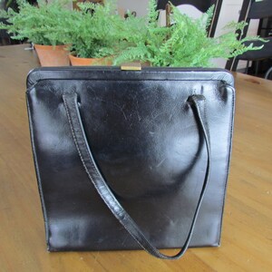 Könnte beinhalten: Eine schwarze Ledertasche mit einem Verschluss und zwei Schultergurten.