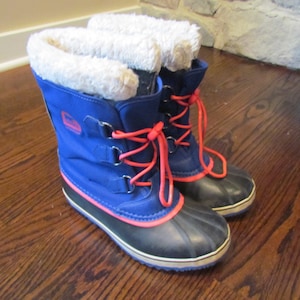 May include: Blue and black winter boots with red laces and a white faux fur lining.