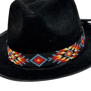 Puede incluir: Un sombrero fedora negro con una banda de cuentas. La banda presenta un patrón geométrico en rojo, naranja, amarillo, azul y blanco.