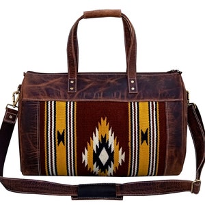 May include: A brown leather duffel bag with a woven tapestry design in shades of red, yellow, white, and black. The bag has a top handle and a long adjustable shoulder strap.