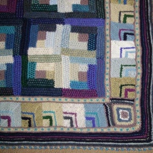 May include: A handmade crochet blanket featuring a patchwork design in shades of blue, purple, green, and cream. The blanket has a square pattern with a border of geometric shapes and a scalloped edge. The blanket is approximately 60 inches by 60 inches.