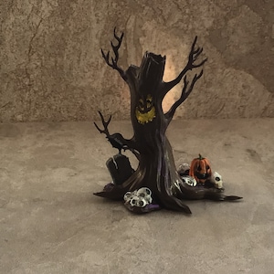 Könnte beinhalten: Ein gruseliger Halloween-Baum mit einem geschnitzten Gesicht, einem Raben, der auf einem Grabstein sitzt, und einem Kürbis mit einem grinsenden Gesicht an der Basis. Der Baum ist von kleinen weißen Schädeln umgeben.