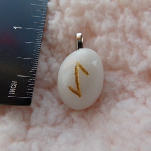 May include: White stone pendant with a gold rune symbol. The pendant is about 1 inch long and has a silver bail.