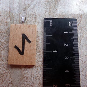 May include: Wooden pendant with a black rune symbol, "Algiz", on a light brown background. The pendant is approximately 1.5 inches tall and has a silver bail.