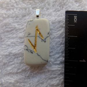 May include: A rectangular pendant with a silver bail. The pendant is white with black veining and a gold-colored rune. The pendant is approximately 1 inch long.