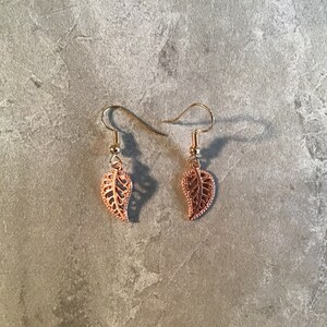 May include: A pair of gold-toned earrings with a delicate leaf design. The leaves are cut out and have a filigree pattern.