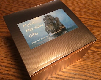 May include: A gold box with a sticker on the top. The sticker has a picture of a ship sailing on the ocean. The text on the sticker reads "Mystic Merchant Gifts" and "Etsy.com/shop/mysticmerchantgifts".