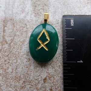 May include: Green oval pendant with a gold-colored bail. The pendant features a gold-colored rune symbol. The pendant is approximately 1 inch in length.