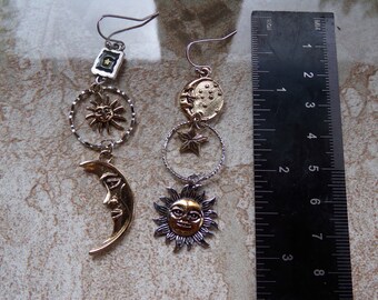May include: A pair of celestial-themed earrings. Each earring features a silver-tone hook, a square with a star, a sun charm, a circular ring, a crescent moon, and a sun pendant. The earrings are approximately 3 inches in length.