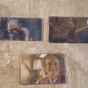 May include: Three framed images of characters from the Lord of the Rings movie series. The first image shows Gollum, a small, green creature with large eyes. The second image shows Gandalf the Grey, a wizard with a long white beard and a pointed hat. The third image shows Bilbo Baggins, a hobbit with a long white beard and a pipe.