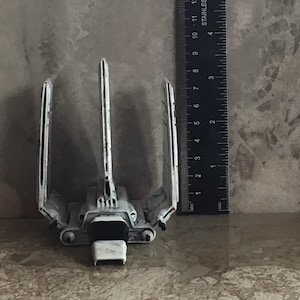 Könnte beinhalten: Ein weißes Modell eines Raumschiffs aus Star Wars mit drei Flügeln. Das Raumschiff ist etwa 15 cm lang und steht auf einer grauen Oberfläche.