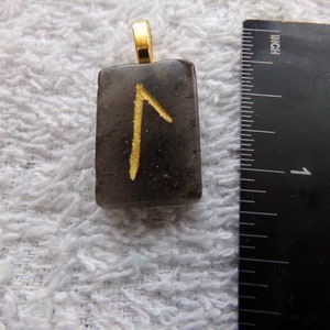 May include: A black stone pendant with a gold rune symbol. The pendant is about 1 inch in size and has a gold bail.