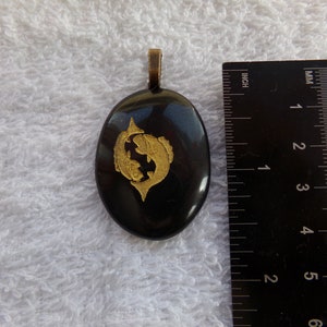 May include: Black oval pendant with a gold Pisces zodiac symbol. The pendant is about 1.5 inches long.