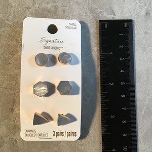 May include: A set of three pairs of earrings featuring different shapes and sizes. The earrings are made of white shell and gold metal. The earrings are displayed on a white card with the text "Signature bead landing" and "3 pairs/paires".
