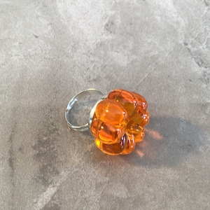 May include: A unique ring featuring a cluster of orange, bubble-like glass beads. The beads are mounted on a silver-colored adjustable band. The ring is set against a gray background.