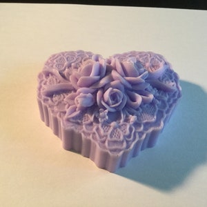 以下が含まれることがあります： ラベンダー色のハート型の装飾ボックス。バラと複雑なレースのような模様のフローラルデザインが特徴です。このボックスはしっかりとした素材でできており、小物入れや装飾品である可能性があります。