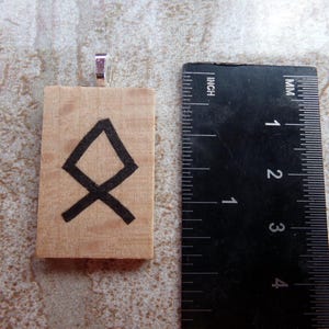 May include: A wooden pendant with a black painted symbol, the Vegvisir, a Norse directional symbol. The pendant is approximately 1.5 inches tall and has a silver bail.