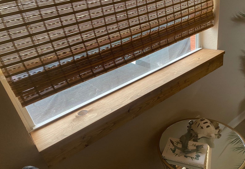 Puede incluir: Un alf&eacute;izar de ventana de madera con una mancha marr&oacute;n claro. El alf&eacute;izar de ventana est&aacute; montado debajo de una ventana con una persiana de bamb&uacute;.