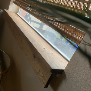 Puede incluir: Un primer plano de un alf&eacute;izar de ventana de madera, te&ntilde;ido de un color marr&oacute;n claro. El alf&eacute;izar est&aacute; montado sobre una ventana con un marco blanco y una persiana de bamb&uacute;.